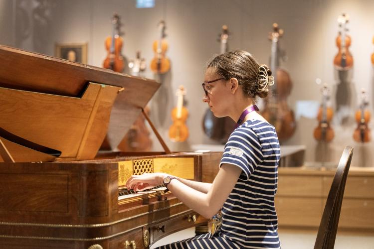 student at piano, violins displayed behind